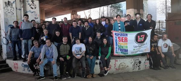 Foto grupal de participantes de la reunión presencial sosteniendo la bandera de la Liga Asperger 7